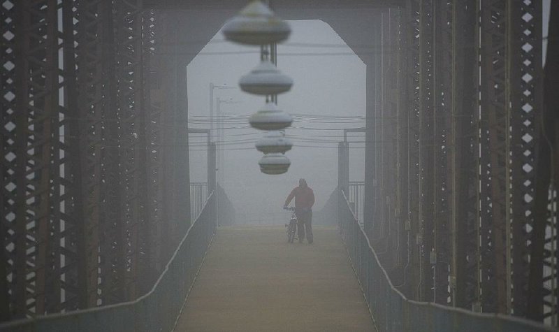 Fredrick Williams Jr. walks across the Clinton Presidential Center Bridge on Wednesday afternoon as fog shrouds the Arkansas River.