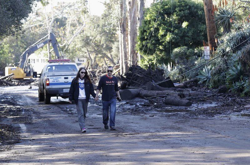 A woman and man walk along a road damaged by storms in Montecito, Calif., Wednesday, Jan. 10, 2018. Dozens of homes were swept away or heavily damaged and several people were killed Tuesday as downpours sent mud and boulders roaring down hills stripped of vegetation by a gigantic wildfire that raged in Southern California last month. (AP Photo/Marcio Jose Sanchez)

