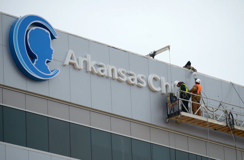 NWA Democrat-Gazette/ANDY SHUPE A worker passes the dot to the letter "I" to another worker on Dec. 29 while assembling a sign from a gondola atop Arkansas Children's Northwest hospital in Springdale.