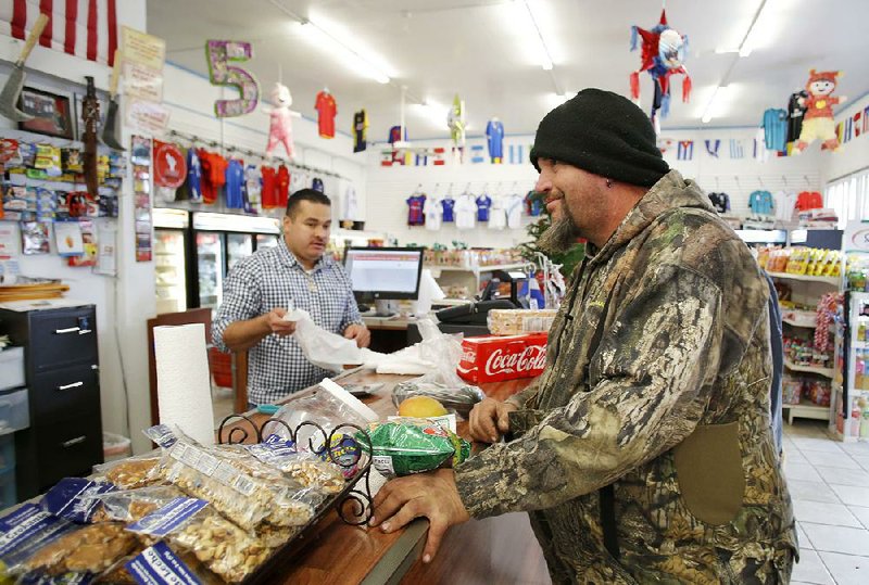 Dale Hunt (right) of Winslow waits at the counter Friday to purchase merchandise and cash his work check at Mercadito Salvadoreno as Jose Merlos, a seven-year employee at the Springdale store, waits on another customer.