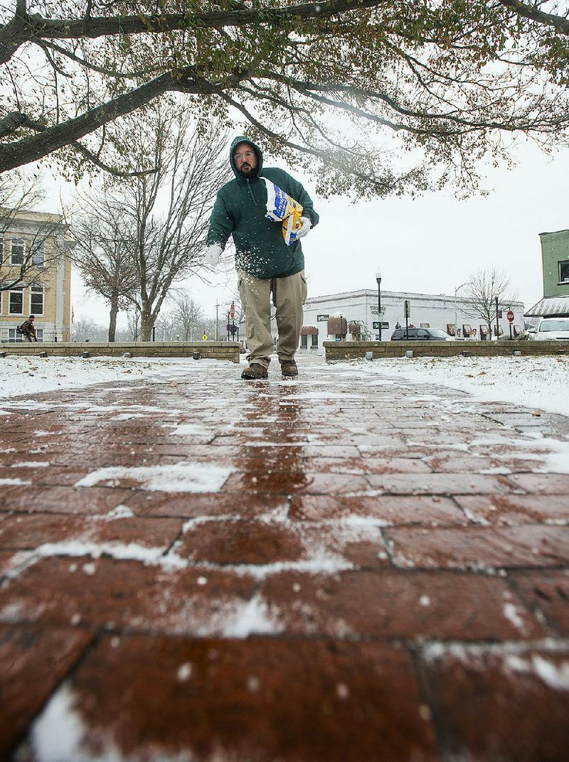 Chris Kester with the Bentonville Parks and Recreation Department spreads salt on the sidewalks Monday around the Bentonville square.