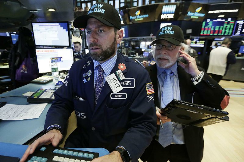 Specialist Michael Pistillo (left), and trader Peter Tuchman wear “Dow 26,000” caps Tuesday as they work on the "oor of the New York Stock Exchange. The Dow brie"y passed the 26,000 benchmark Tuesday before falling to 25,792.86 at closing.  
