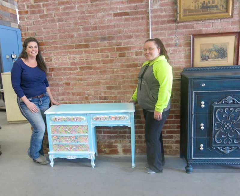 WESTSIDE EAGLE OBSERVER/Susan Holland Dawn Dawson (left), owner of White Horse Designs by Dawn, and her partner, Aubrey Doss, display a dressing table they recently refinished at her workshop at 104 Main Street N.E. in Gravette. The piece was painted and powder glazed in pastel colors in preparation for use in a teenage girl's bedroom. The ladies invite area residents to contact them with any furniture refinishing or restoration projects they want done.