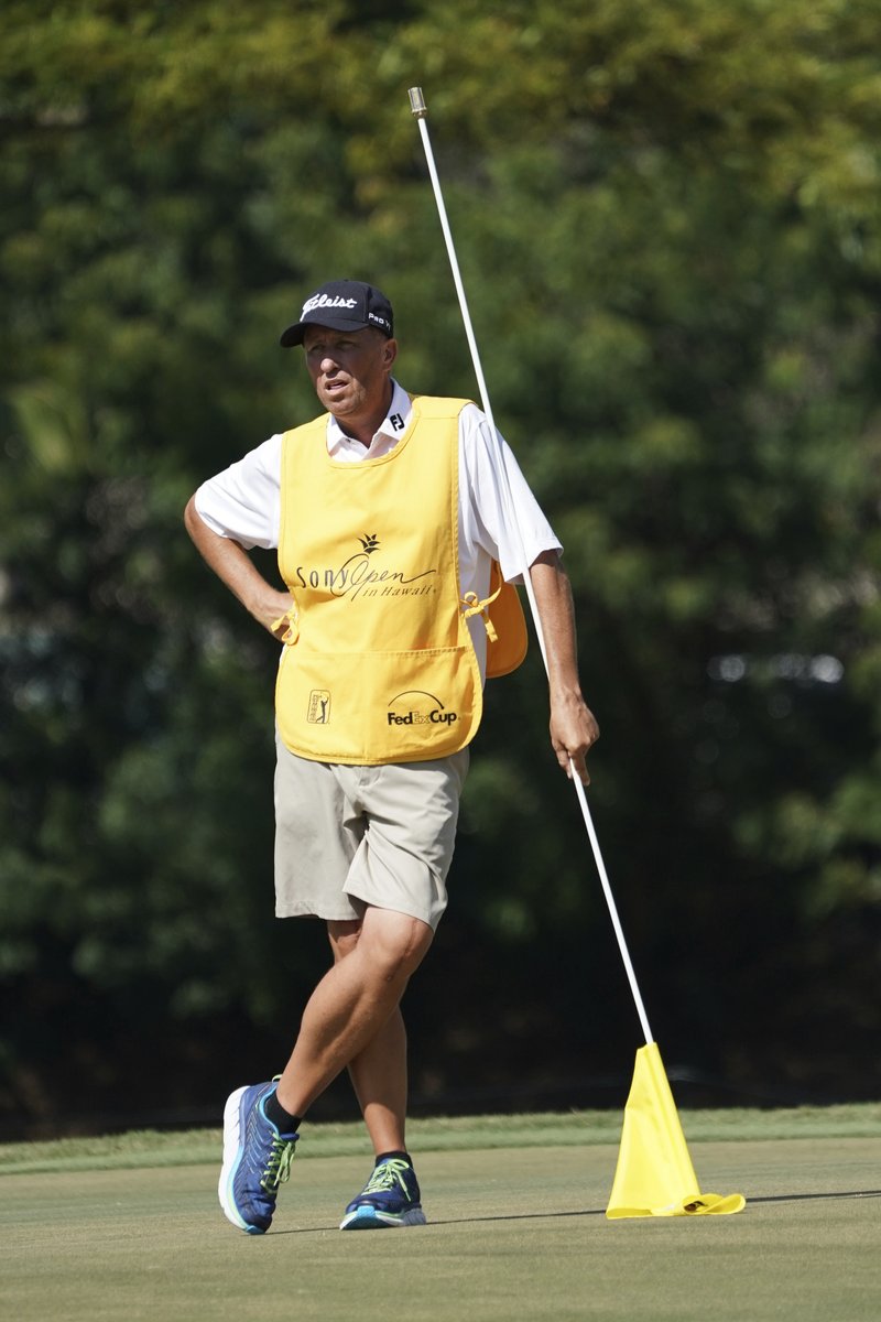 While leaning on the pin flag, Jim "Bones" Mackay stands on the seventh green during the third round of the Sony Open golf tournament, Saturday Jan. 13, 2018, in Honolulu. Although he retired last year, MacKay is filling in for Justin Thomas' injured caddie. (AP Photo/Marco Garcia)