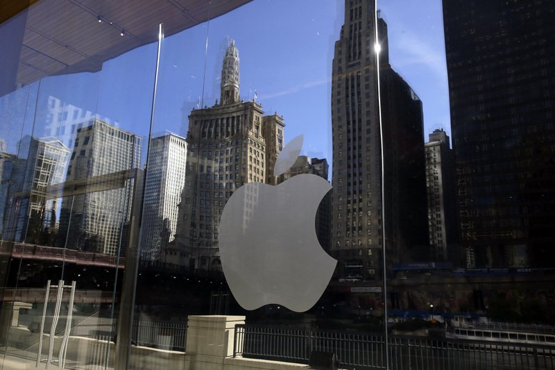 FILE - In this Thursday, Oct. 19, 2017, file photo, buildings and a tour boat are reflected on the mirror behind an Apple logo during a preview event at a new Apple Michigan Avenue store, in downtown Chicago. On Wednesday, Jan. 17, 2018, Apple announced it is planning to build another corporate campus and hire 20,000 workers during the next five years as part of a $350 billion commitment to the U.S. economy. (AP Photo/Kiichiro Sato, File)