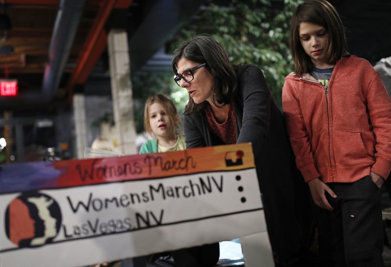 In this Jan. 17, 2018, photo, Minnie Wood, center, makes signs with her daughters Buckley, right, and Zoey in preparation for a rally in Las Vegas. A year after more than 1 million people rallied at women's marches around the world with a message of female empowerment and protest of President Donald Trump, organizers will mark the anniversary with more than a hundred marches around the world and a rally in Las Vegas aiming to channel the activism to register voters and swing elections for progressives this year. (AP Photo/John Locher)