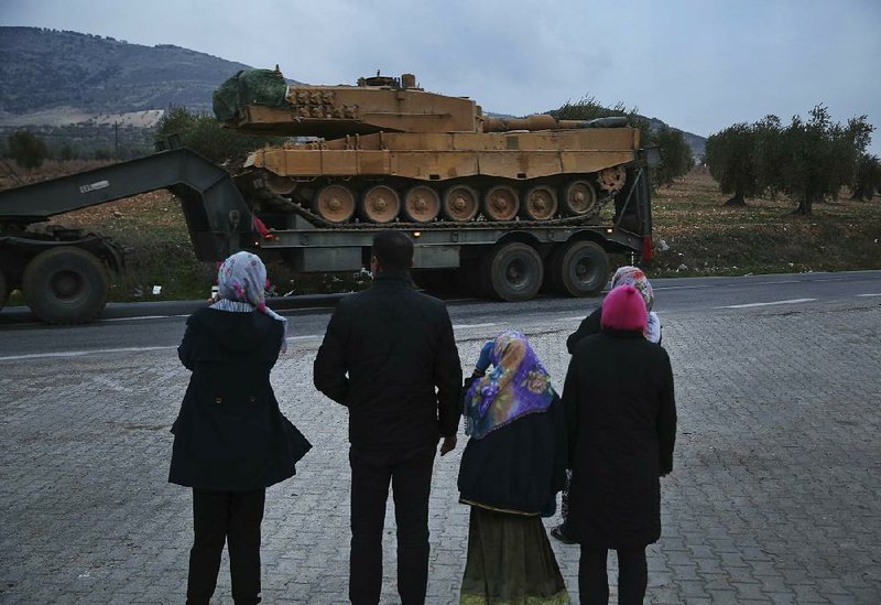 Residents watch as a truck, part of a convoy, transporting a Turkish army tank passes Sunday through the town of Kilis, Turkey.
