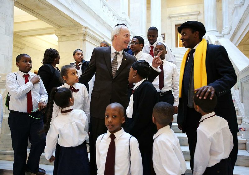 Arkansas Gov. Asa Hutchinson (center) talks to pastor Aaron Agnew, director of Word of Outreach Christian Academy, after posing for a photo with academy students Wednesday during the School Choice Rally at the Capitol. 