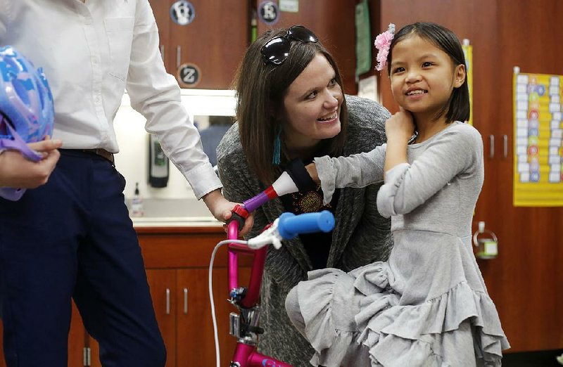 Julie Marvin watches as her daughter Gracie, a first-grader at Willis D. Shaw Elementary School, places her arm in the new prosthetic attached to the handlebars of her bicycle Tuesday at the school in Springdale. 