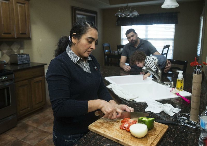 Maria Sanabria prepares a meal Thursday as her husband, Jose, plays with their daughter, Elena, in Centerton. Jose Sanabria said “it’s hard to really give an answer” when he was asked about his status as federal protections for Salvadorans are set to expire. 