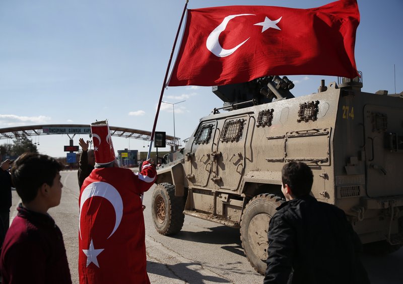 In support of the Turkish forces' offensive, codenamed 'Olive Branch' in the Kurdish-controlled enclave of Afrin, Syria, Isikli Tosun Baba, 60, dressed in a Turkish flag, waves one as a Turkish forces armoured personnel carrier is driven past, at the Oncupinar border crossing with Syria, known as Bab al Salameh in Arabic, in the outskirts of the town of Kilis, Sunday, Jan. 28, 2018. 