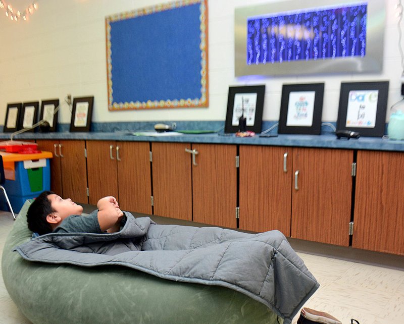 Daniel Tello, a kindergarten student at Northside Elementary School in Siloam Springs, snuggles inside a peapod bed under a weighted blanket as he watches the bubble wall inside the school’s new sensory room.