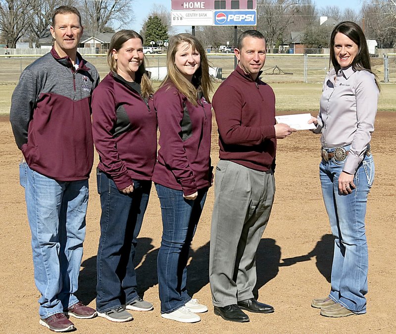 Westside Eagle Observer/RANDY MOLL Savannah Dickinson, vice president and branch manager of Farm Credit of Western Arkansas (right), presents a check to Brae Harper, Gentry High School principal and athletic director, for the purchase of a new scoreboard for the softball field in the Merrill Reynolds Memorial Complex at the high school on Friday. Dickinson and Harper were accompanied on the softball field by head softball coach Paul Ernest and assistant coaches Ayla Smartt and Erica Jones.
