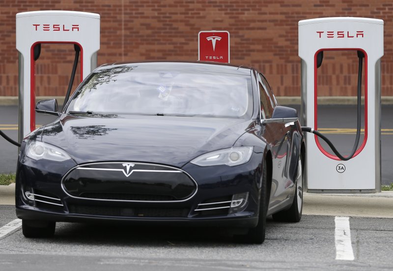 FILE- In this June 24, 2017, file photo, a Telsa car recharges at a Tesla charging station at Cochran Commons shopping center in Charlotte, N.C. (AP Photo/Chuck Burton)