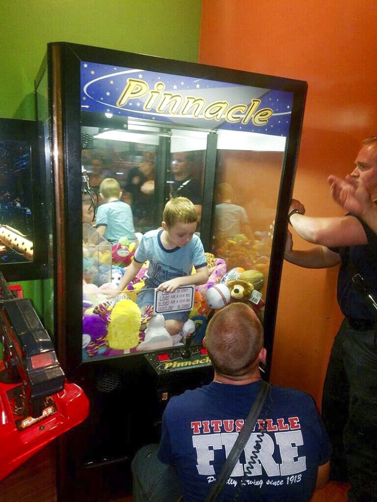 This photo made available by the Titusville Fire and Emergency services shows fire fighters attempting to rescue a boy who crawled inside a claw-style vending machine, Wednesday, Feb. 7, 2018, in Titusville, Fla. The boy sat atop the stuffed toys while firefighters took just 5 minutes to get him out. 