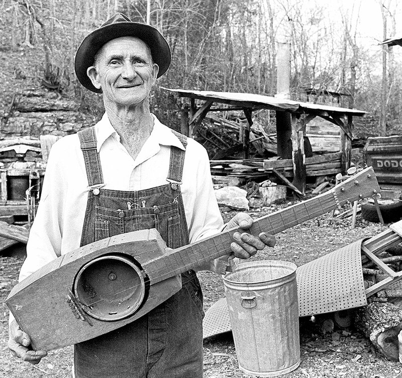 Ed Stilley, who spent his life building handmade instruments for children near Hogscald Holler in Madison County, poses with one of his guitars late in his body of work. Stilley is the subject of Kelly Mulhollan’s book, “True Faith, True Light: The Devotional Art of Ed Stilley,” and an exhibit at the Old State House Museum.