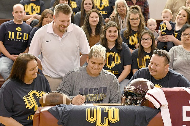 Bud Sullins/Special to the Herald-Leader Oaks-Mission (Okla.) senior lineman Joseph &quot;Choogie&quot; Young signed a letter of intent Friday to play football at the University of Central Oklahoma in the Oaks gymnasium. Also pictured are his mother Penny, left, and father Chero, right, Oaks head football coach C.D. Thompson, standing, and a host of friends and family.