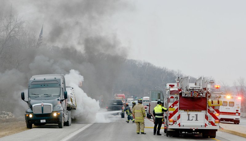 Keith Bryant/The Weekly Vista Bella Vista and White Rock firefighters work to put out a fire that appeared to start in the rear axle of a trailer pulled by a semi-tractor on U.S. Highway 71, just north of the state line. Emergency workers had to stop southbound traffic on the interstate to put out the fire on a chilly Tuesday. "When these tires catch on fire, it always looks worse than it is," said Bella Vista deputy chief Bryan Wolfgang.