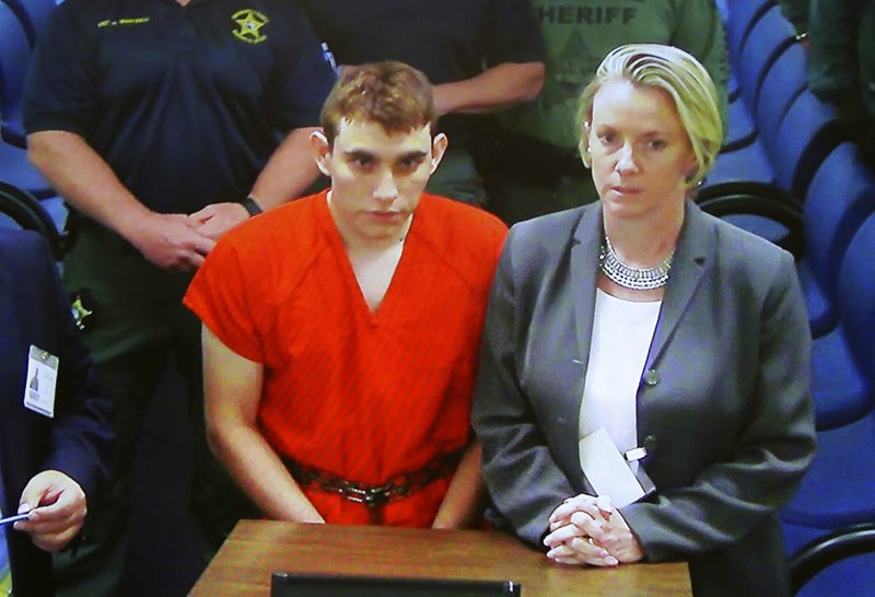 A video monitor shows school shooting suspect Nikolas Cruz, left, making an appearance before Judge Kim Theresa Mollica in Broward County Court, Thursday, Feb. 15, 2018, in Fort Lauderdale, Fla.  Cruz is accused of opening fire Wednesday at the school killing more than a dozen people and injuring several.