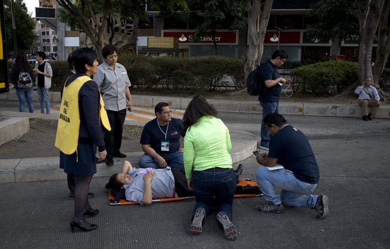 A woman is helped outside, along Reforma Avenue after a 7.2-magnitude earthquake shook Mexico City, Friday, Feb. 16, 2018. A powerful earthquake has shaken south and central Mexico, causing people to flee buildings and office towers in the country's capital, and setting off quake alert systems. (AP Photo/Eduardo Verdugo)