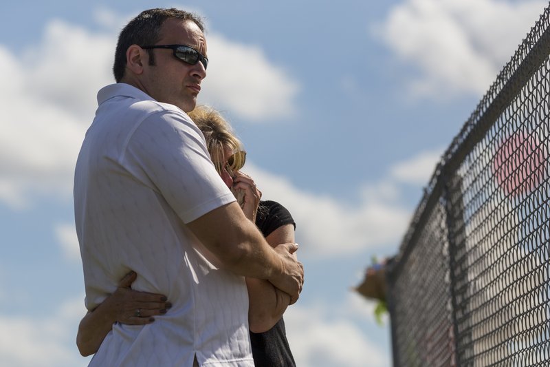 Mourners hug near a makeshift memorial created by community members outside of Marjory Stoneman Douglas High School in Parkland, Fla., on Sunday, Feb. 18, 2018. A gunman entered the school last Wednesday and killed 17 students and teachers. (Matias J. Ocner/Miami Herald via AP)