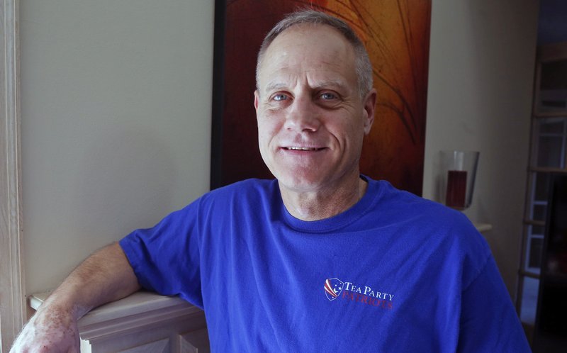 In this Feb. 16, 2018, photo, Andy Cilek poses with a Tea Party shirt at his home in Eden Prairie, Minn. Cilek was one of two voters who defied elections officials after he was asked to cover up a tea-party shirt and button. A Minnesota law that bars voters from wearing political hats, T-shirts, buttons and other apparel to the polls is about to get a look from the Supreme Court. (AP Photo/Jim Mone)