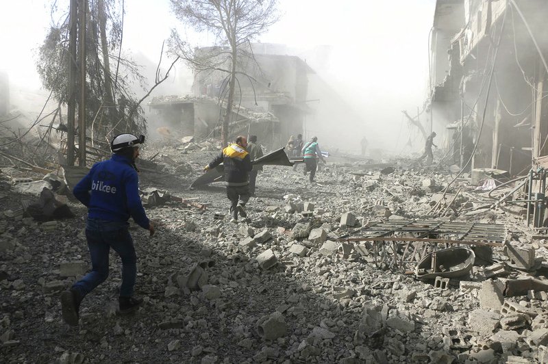 In this photo released Tuesday Feb. 20, 2018 which provided by the Syrian Civil Defense group known as the White Helmets, shows members of the Syrian Civil Defense run to help survivors from a street that attacked by airstrikes and shelling of the Syrian government forces, in Ghouta, suburb of Damascus, Syria. 