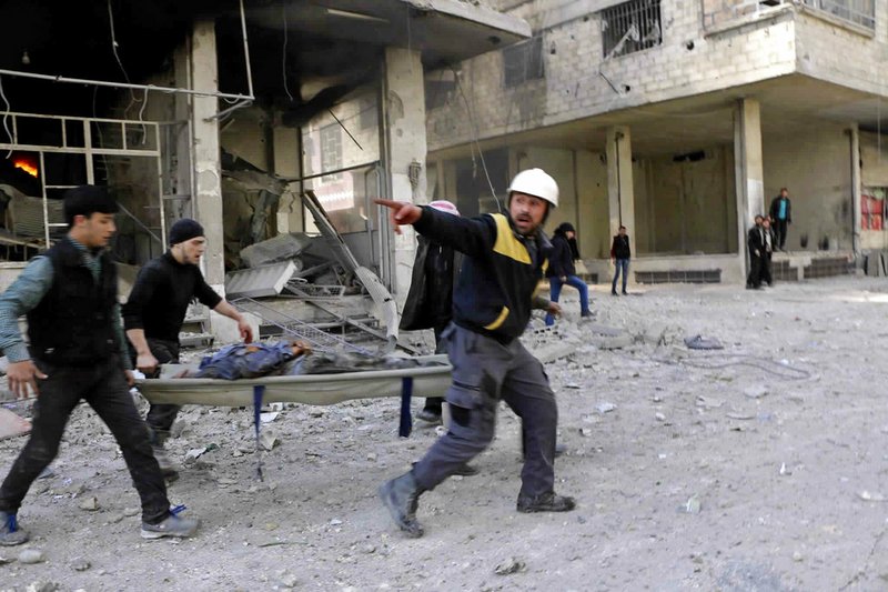 This photo released Tuesday Feb. 20, 2018, provided by the Syrian Civil Defense group known as the White Helmets, shows members of the Syrian Civil Defense group carrying a man who was wounded  during airstrikes and shelling by Syrian government forces, in Ghouta, a suburb of Damascus, Syria. Intense Syrian government shelling and airstrikes of rebel-held Damascus suburbs killed at least 100 people since Monday in what was the deadliest day in the area in three years, a monitoring group and paramedics said Tuesday.