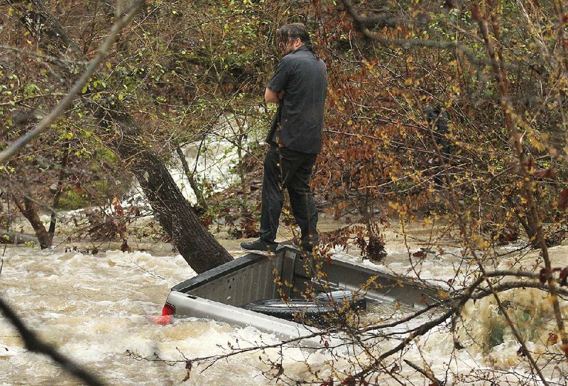 A man stands on the back of a pickup after getting stranded while trying to cross high water just off Mill Creek Road in Hot Springs. The truck later was swept under, but the man jumped to safety. 