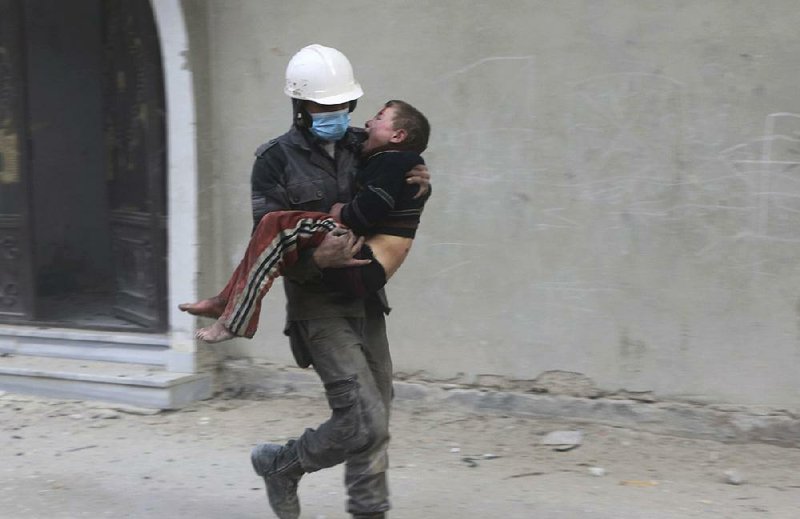 A member of the Syrian civil defense group known as the White Helmets carries a boy injured during Wednesday’s airstrikes in Ghouta in this photo provided by the rescue group. 