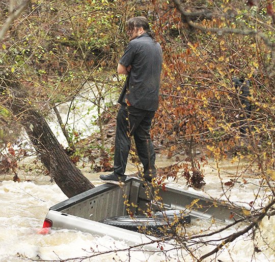 The Sentinel-Record/Richard Rasmussen SWEPT AWAY: Jonathan Werst of Holy Spirit Loop makes his way to safety through floodwaters early Wednesday after his Chevrolet Silverado pickup truck was swept into the Middle Branch of Gulpha Creek. The sequence of photographs, below in story, shows his escape from the bed of his flooded truck.