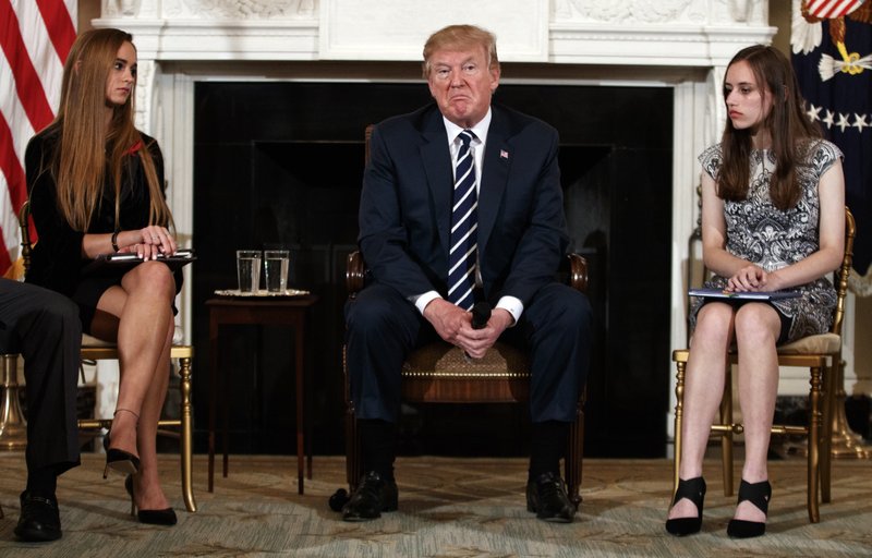 President Donald Trump, joined by Marjory Stoneman Douglas High School student Carson Abt, right, and Julia Cordover, the student body president at Marjory Stoneman Douglas High School, left, pauses during a listening session with high school students teachers, and others in the State Dining Room of the White House in Washington, Wednesday, Feb. 21, 2018. (AP Photo/Carolyn Kaster)