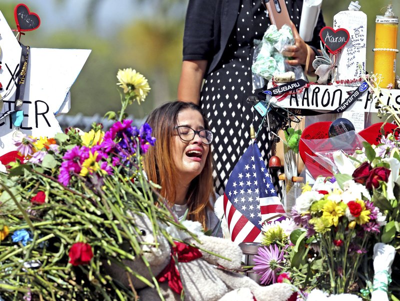 Marjory Stoneman Douglas High School former student Ariana Gonzalez weeps at a cross of slain Marjory Stoneman Douglas coach Aaron Feis, on a hill honoring those killed, Friday, Feb. 23, 2018, in Parkland, Fla. Teachers and staff returned to the school, to begin to organize and prepare to welcome students next week. Over a dozen students and teachers were killed on Valentine's Day in a mass shooting at the high school. (Charles Trainor Jr./Miami Herald via AP)