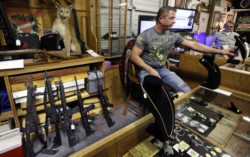 In this photo taken Oct. 20, 2017, Johnny's Auction House owner John West prepares items, including a line of assault rifles behind, for auction where the company handles gun sales for both civilians and a half dozen police departments and the Lewis County Sheriff's Office, in Rochester, Wash. When Washington state and other law enforcement agencies across the country sell guns they've confiscated during criminal investigations, they're not just selling pistols and hunting rifles, they're also putting assault weapons, including AR-15s, back on the street. 