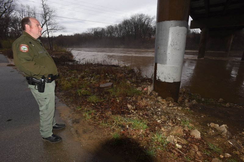 Clayton Hungate, a wildlife officer with the Arkansas Game and Fish Commission, watches Saturday the White River flows swiftly under the Arkansas 45 bridge at Goshen. The river, a tributary of Beaver Lake, was bank-full Saturday in the wake of more rain.