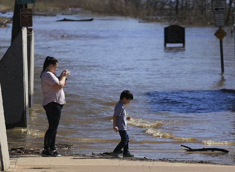 Kelli Fletcher and her son Gabriel Gomez, 6, look at the floodwater covering the Arkansas River Trail at the foot of the Big Dam Bridge on Monday afternoon in North Little Rock. The surging Arkansas River has overflowed part of the trail, and more rain is expected in Little Rock in the coming days.