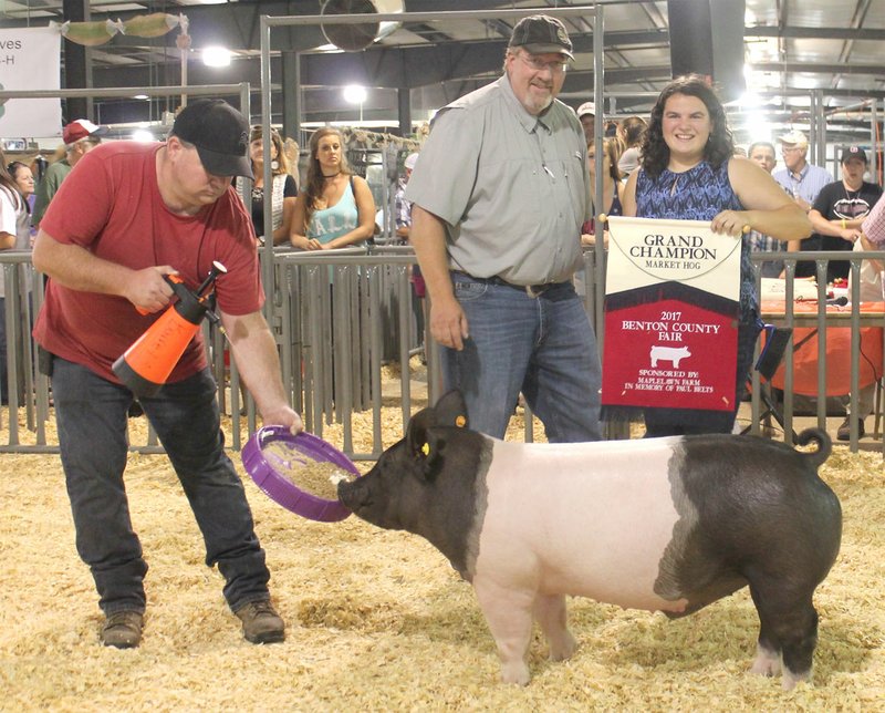 Westside Eagle Observer/SUBMITTED Paige Barrett (right) receives a Grand Champion banner from judge Brian Anderson (center) after winning the Benton County Youth Livestock show's Grand Champion Market hog award at the Benton County Fair in Bentonville Aug. 11, 2017.
