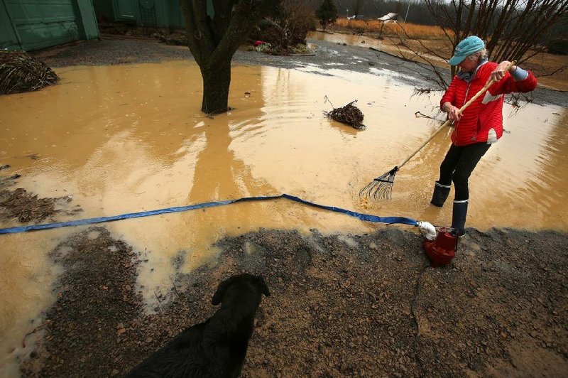 Sandy Wilson rakes up debris Wednesday before pumping out her yard in Pangburn after a pond levee broke and sent water rushing past her house and into the Little Red River. She said much of the damage was in the garage, where the water left behind a couple of feet of mud. 