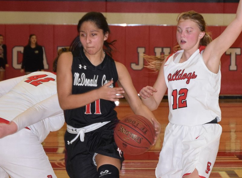 RICK PECK/SPECIAL TO MCDONALD COUNTY PRESS McDonald County's Rita Santillan splits Carl Junction's Megan Scott (42) and Shila Winder (12) on her way to the basket during the Lady Mustangs' 51-23 loss on Feb. 22 at Carl Junction High School.