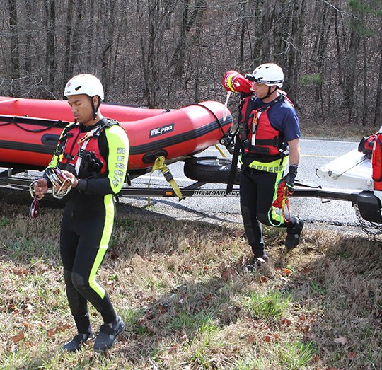 The Sentinel-Record/Richard Rasmussen TEAM MEMBERS: Hot Springs Fire Department swift water rescue team members Trey Hicks, left, and Larry Vincent carry equipment to a creek behind 7162 Central Ave., about one and a half miles south of the Garland County line, in Hot Spring County on Thursday.