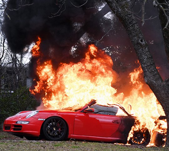 The Sentinel-Record/Grace Brown - a red Porsche burns in the back yard of 217 Laser Street after catching fire shortly before 3 p.m. on Sunday, March 4, 2018. According to the owner, the vehicle caught fire in the garage and he pushed it out bfore it destroyed his home. He waid he bought the vehicle about three weeks ago. 