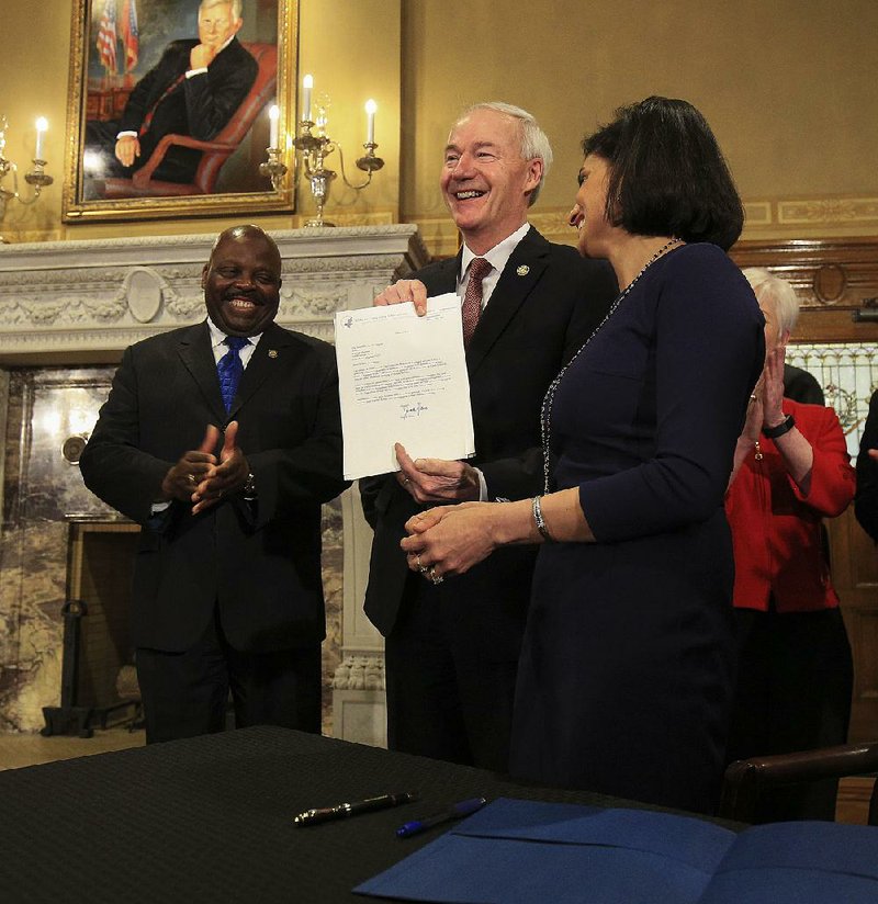 Centers for Medicare and Medicaid Services Administrator Seema Verma (right) on Monday makes a rare personal delivery to Gov. Asa Hutchinson (center) of a federal waiver allowing Arkansas to require participants in the state’s expanded Medicaid program to work or be involved in work-related activities in order to qualify for the government-sponsored health insurance. Arkansas Department of Workforce Services Director Daryl Bassett (left) applauded.