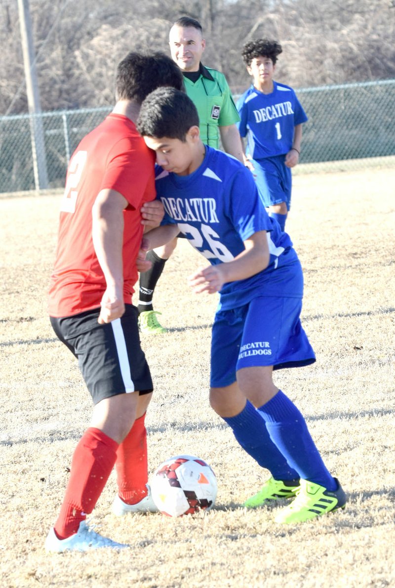 Westside Eagle Observer/MIKE ECKELS Jason Orellana (Decatur 26) and a Pirate player go head to head over a loose ball during the March 1 Decatur-Locust Grove boys' soccer match at Bulldog Stadium in Decatur. The varsity boys won their first match of the season with an 11-0 shutout of Locust Grove.