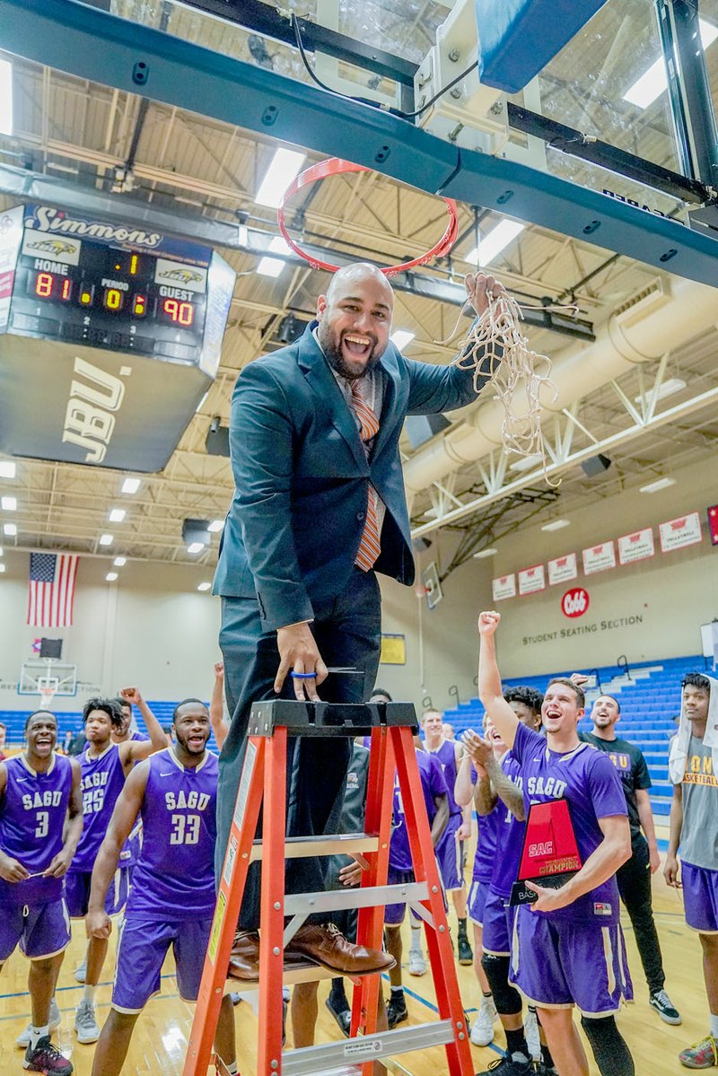 Matthew Christensen/JBU Sports Information First-year Southwestern Assemblies of God coach Delton Deal holds up the freshly trimmed basketball net after the Lions defeated Wayland Baptist 90-81 on Saturday in the Sooner Athletic Conference Tournament men's championship at Bill George Arena on the campus of John Brown University.