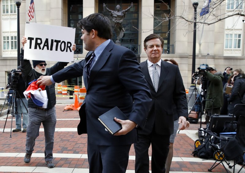 Jason Maloni, the spokesman for former Trump campaign chairman Paul Manafort, left, throws a Russian flag back at protester Bill Christeson, left with sign, after he threw it at Paul Manafort, right, while leaving Alexandria federal courthouse after an arraignment hearing in Alexandria, Va., Thursday, March 8, 2018. (AP Photo/Jacquelyn Martin)