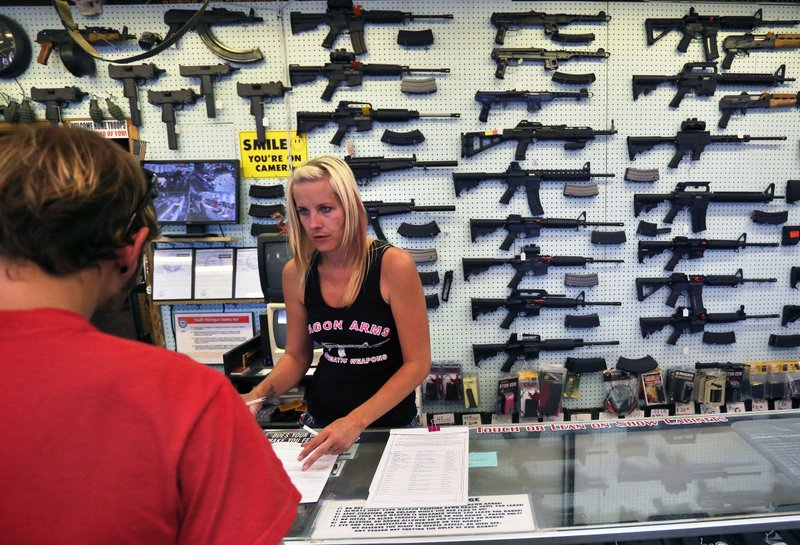 In this July 20, 2014, file photo, with guns displayed for sale behind her, a gun store employee helps a customer at Dragonman's, east of Colorado Springs, Colo. Recent mass shootings spurred Congress to try to improve the background check system used during gun purchases, but experts say the system is so fractured that federal legislation being considered in Washington D.C. will do little to help keep weapons out of the hands of dangerous people. 