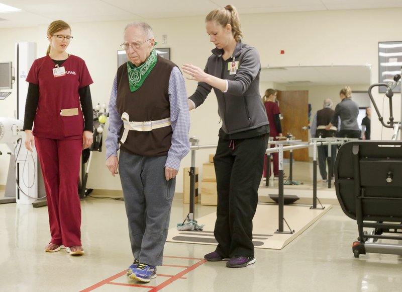 NWA Democrat-Gazette/DAVID GOTTSCHALK Edward VanDuzer (center) is assisted by Heather Vaughn (left), physical therapist, and Sharina Cassity, physical therapy student, during a balance and mobility exercise at the University of Arkansas for Medical Sciences Northwest Outpatient Therapy Clinic in Fayetteville. The physical therapy program is new and the first 24 students are expected to graduate in May.