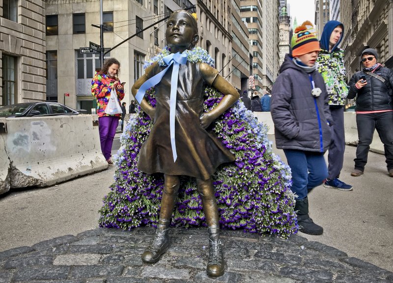 Wall Street's "Fearless Girl" statue is draped with a bouquet of flowers to mark International Women's Day, Thursday March 8, 2018, in New York. The statue, which has been a New York City tourist attraction since it was installed to mark International Women's Day one year ago, is staying put for now while city officials figure out where it's going next to spread its message of female empowerment. (AP Photo/Karen Matthews)