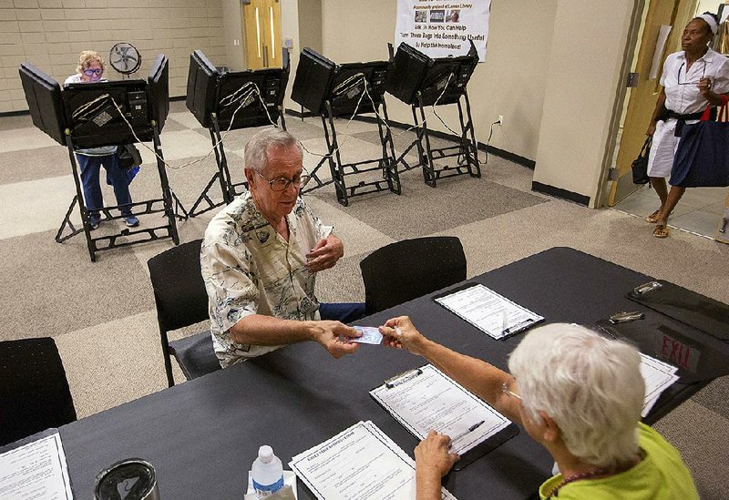 Ken Bushe hands a photo ID to a poll worker at Laman Library in North Little Rock during voting for a North Little Rock sales-tax increase in August. It was the first election after the voter-ID law went into effect.
