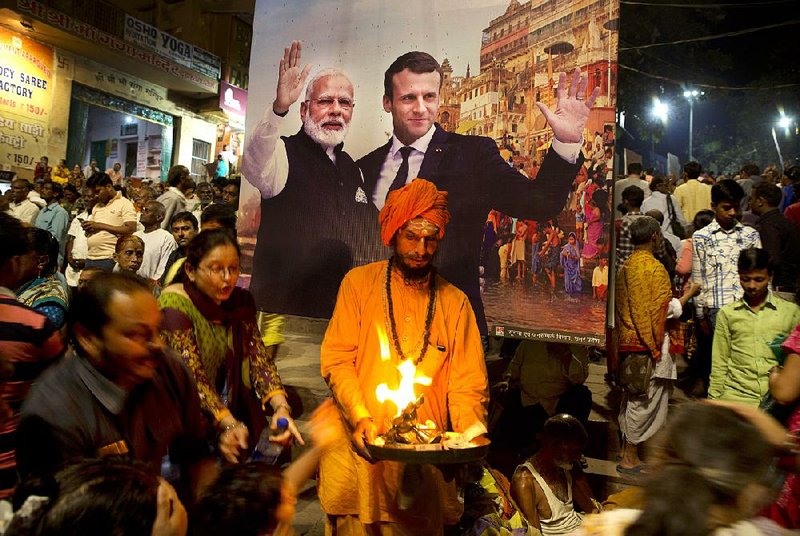 A Hindu holy man offers blessings Sunday in Varanasi, India, beneath a banner welcoming Indian Prime Minister Narendra Modi (left) and French President Emmanuel Macron.